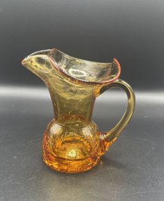 a yellow glass pitcher sitting on top of a table next to a gray wall and floor