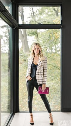 a woman standing in front of a window holding a pink purse and looking at the camera