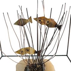 three metal fish sitting on top of a plant in a vase filled with dirt and twigs