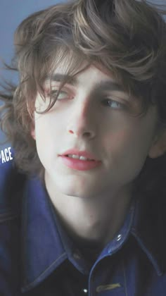 a young man with curly hair and blue shirt looking at the camera while wearing a denim jacket