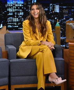 a woman sitting on top of a blue couch in front of a tv screen wearing a yellow suit