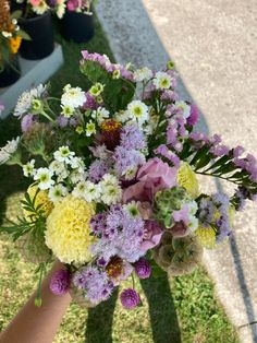 a person holding a bouquet of flowers in their hand on the grass near some potted plants