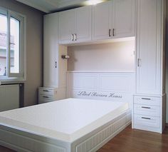 an image of a bed in a room with white cabinets and drawers on the wall