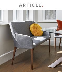 a grey chair with a yellow pillow sitting on top of it next to a glass table