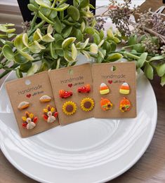 three small earrings are sitting on a plate next to some flowers and plants in the background