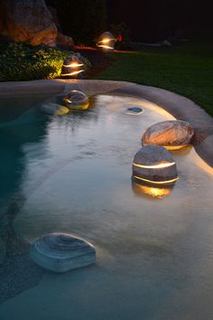 some rocks are lit up by lights in the water and on the side of a pool