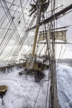 an old sailing ship in rough seas with the sails down and water splashing around it