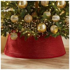 a christmas tree with ornaments and lights in a red potted planter on a wooden floor