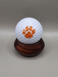 a white golf ball with an orange paw print on the front and bottom, sitting on a wooden stand