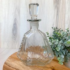 a clear glass bottle sitting on top of a wooden table next to a potted plant