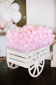 a wagon filled with pink cotton balls on top of a wooden floor next to balloons