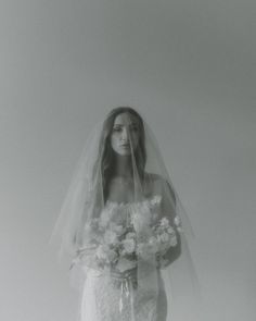 a woman in a wedding dress with flowers on her veil, standing against a white background