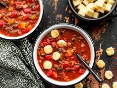 two bowls filled with soup next to some crackers and cheese on a table top