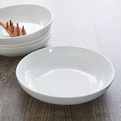 three white bowls with toothbrushes in them on a wooden table top next to each other