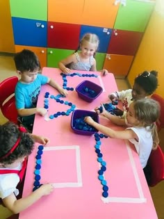 several children sitting at a table with blue beads