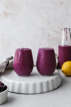 two glasses filled with blueberry smoothie next to lemons and raspberries