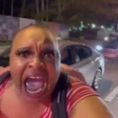 a woman with her mouth wide open in front of a car and another person taking a selfie