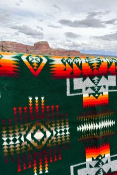 the blanket is green, orange and white with designs on it in front of mountains