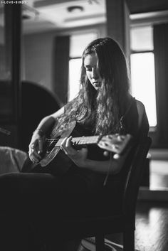 a woman sitting in a chair playing a guitar