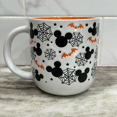 a mickey mouse mug with bats and spider webs on it, sitting on a counter