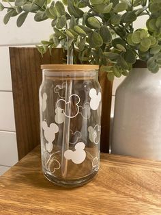 a glass vase with mickey mouse decals on it sitting on a table next to a potted plant