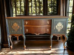 an ornately painted desk sits in front of large windows with wood trimmings