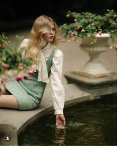 a woman is sitting on the edge of a fountain with flowers in her hair and wearing a green dress