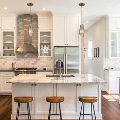 two stools sit at the center of this kitchen island with marble countertops and stainless steel appliances