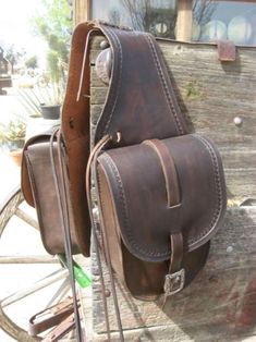 two brown leather saddles sitting next to each other on a wooden bench in front of a window