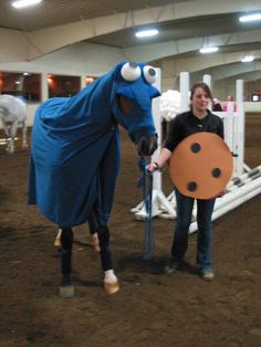 a woman standing next to a horse wearing a blue blanket and holding a brown stick