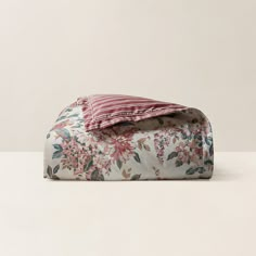 an unmade bed with floral print on it and a striped pillow case in the corner