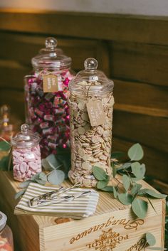 there are many different types of candies in glass jars on top of a wooden box