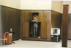 a man in a suit standing on top of a wooden cabinet next to a desk