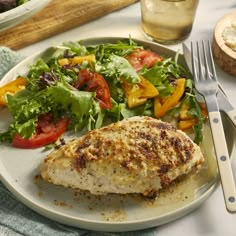 a white plate topped with meat and salad next to a glass of water on top of a table