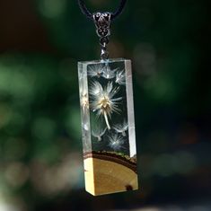 a dandelion in a glass block hanging from a black cord with a bead