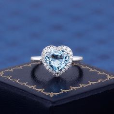 a heart shaped diamond ring sitting on top of a black box with a blue background