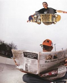 a man sitting on the ground reading a newspaper while holding a skateboard above his head