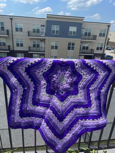 a purple crocheted blanket hanging from a metal railing in front of a building