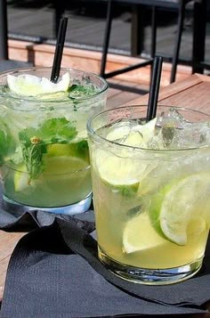 two glasses filled with lemonade and lime on top of a wooden table