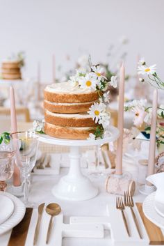 there is a cake on the table with flowers and candles around it, as well as other place settings