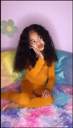 a young woman sitting on top of a bed with long black hair and wearing an orange outfit