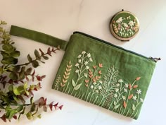 a green pouch with flowers on it next to a plant and a small embroidered coin purse