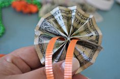 a person is holding a fan made out of dollar bills and orange ribbon on the end