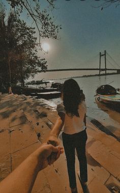 two people holding hands near the water with boats on the shore in the background at night