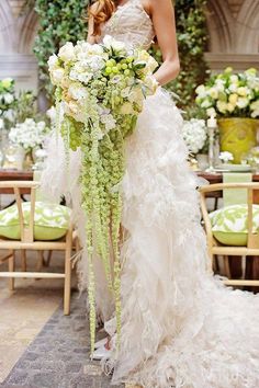 a woman in a wedding dress holding a large flower bouquet with greenery on it