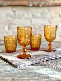 four yellow glass goblets sitting on top of a wooden table next to a brick wall