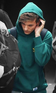 a young man in a green hoodie is holding his head to his ear as he walks