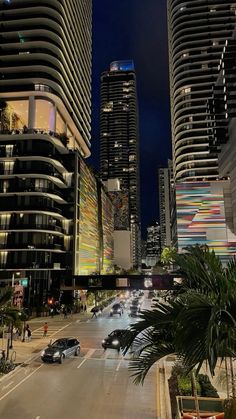 a city street at night with tall buildings and palm trees in the foreground, cars driving on the road