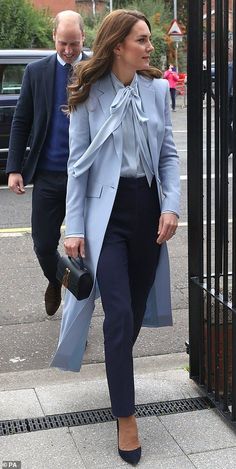 the woman is walking down the sidewalk with her hand in her pocket and wearing a blue coat