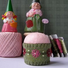 two gnomes sitting on top of a cupcake next to some thread spools